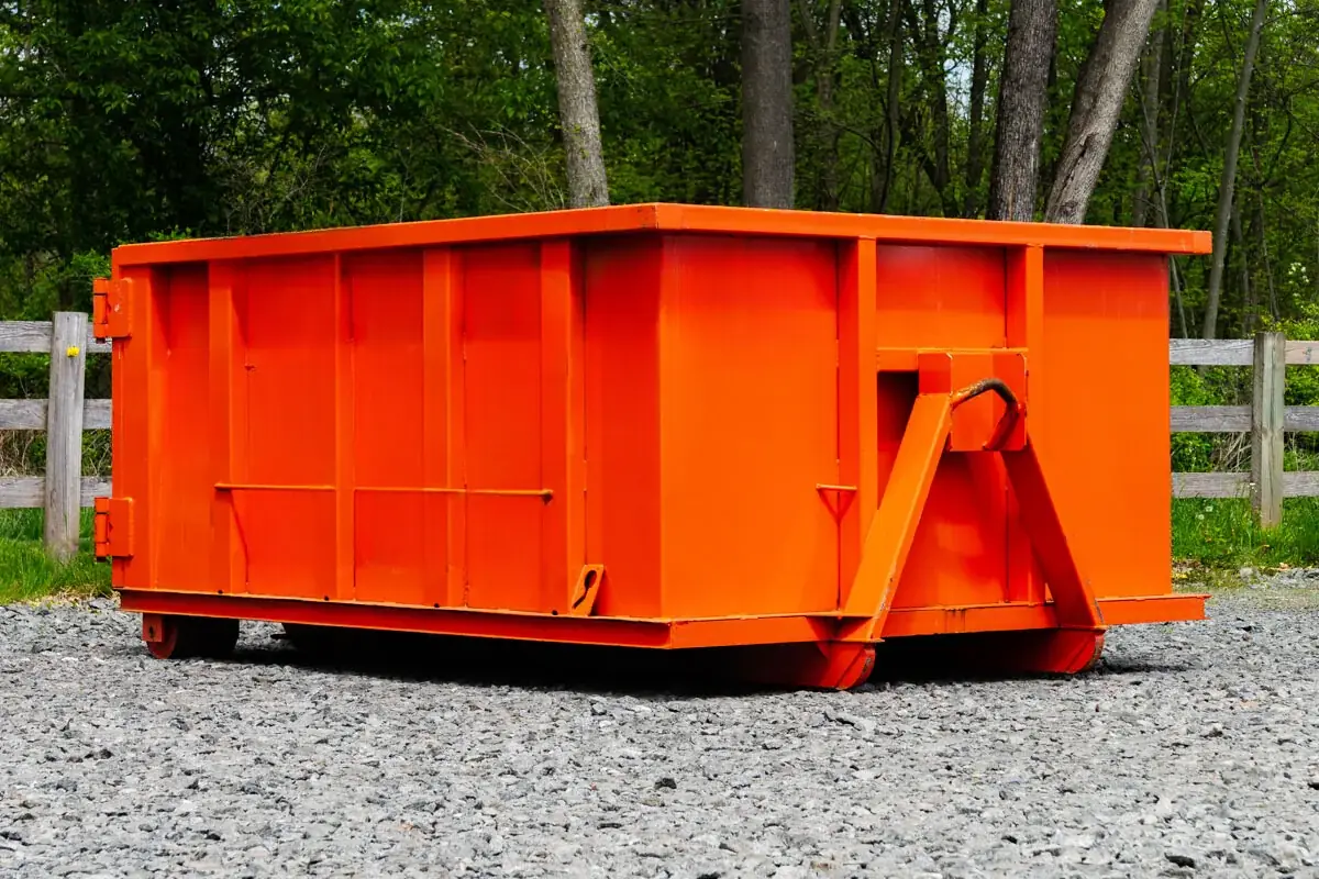 Short orange roll-off dumpster on gravel