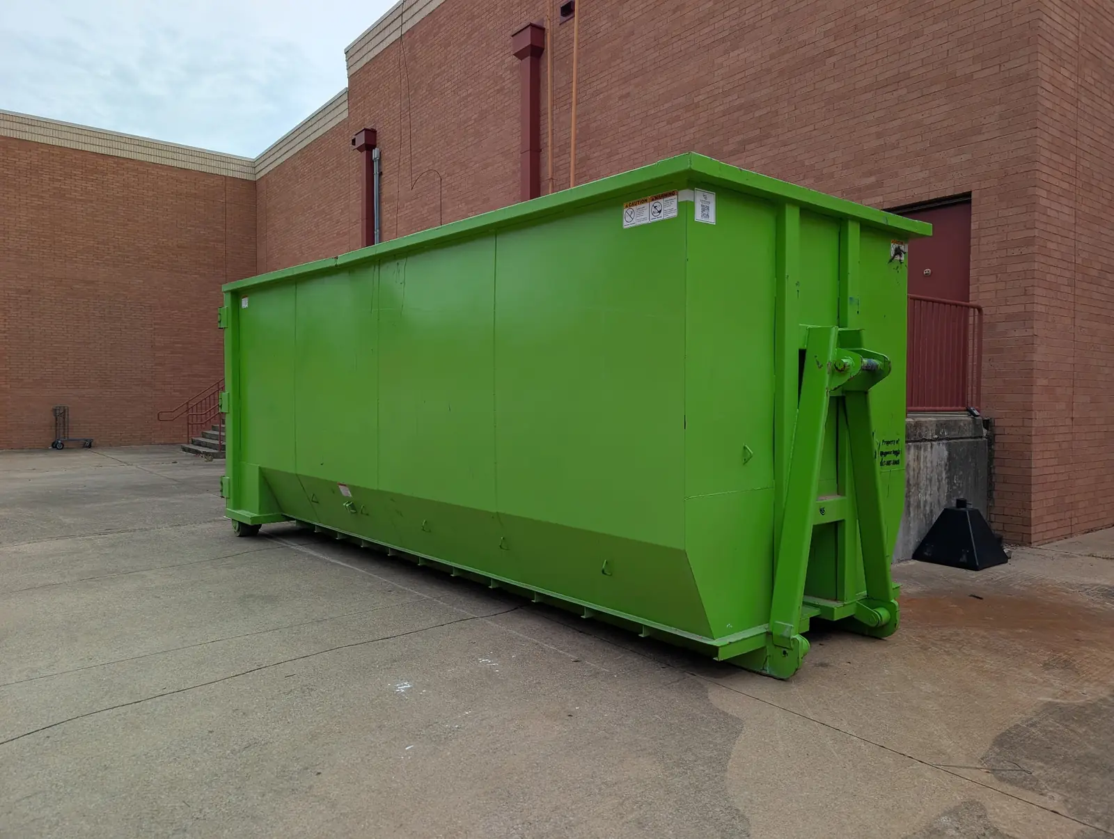 Green roll-off dumpster beside a brick commercial building